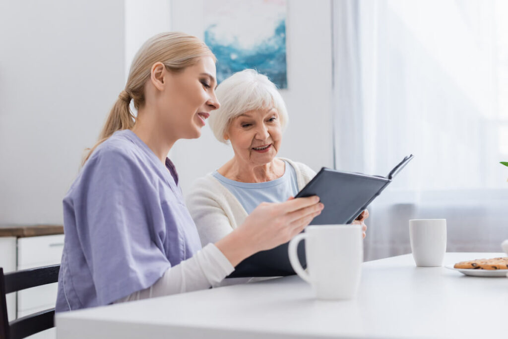 Proveer at Grande View | Happy senior and caregiver looking at photo album in kitchen